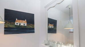 Een badkamer met een schilderij van een huis, een spiegel en een plank met glazen.
