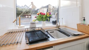 Een keuken met een raam, een spoelbak, een afwasschaal en een vaas met bloemen.
