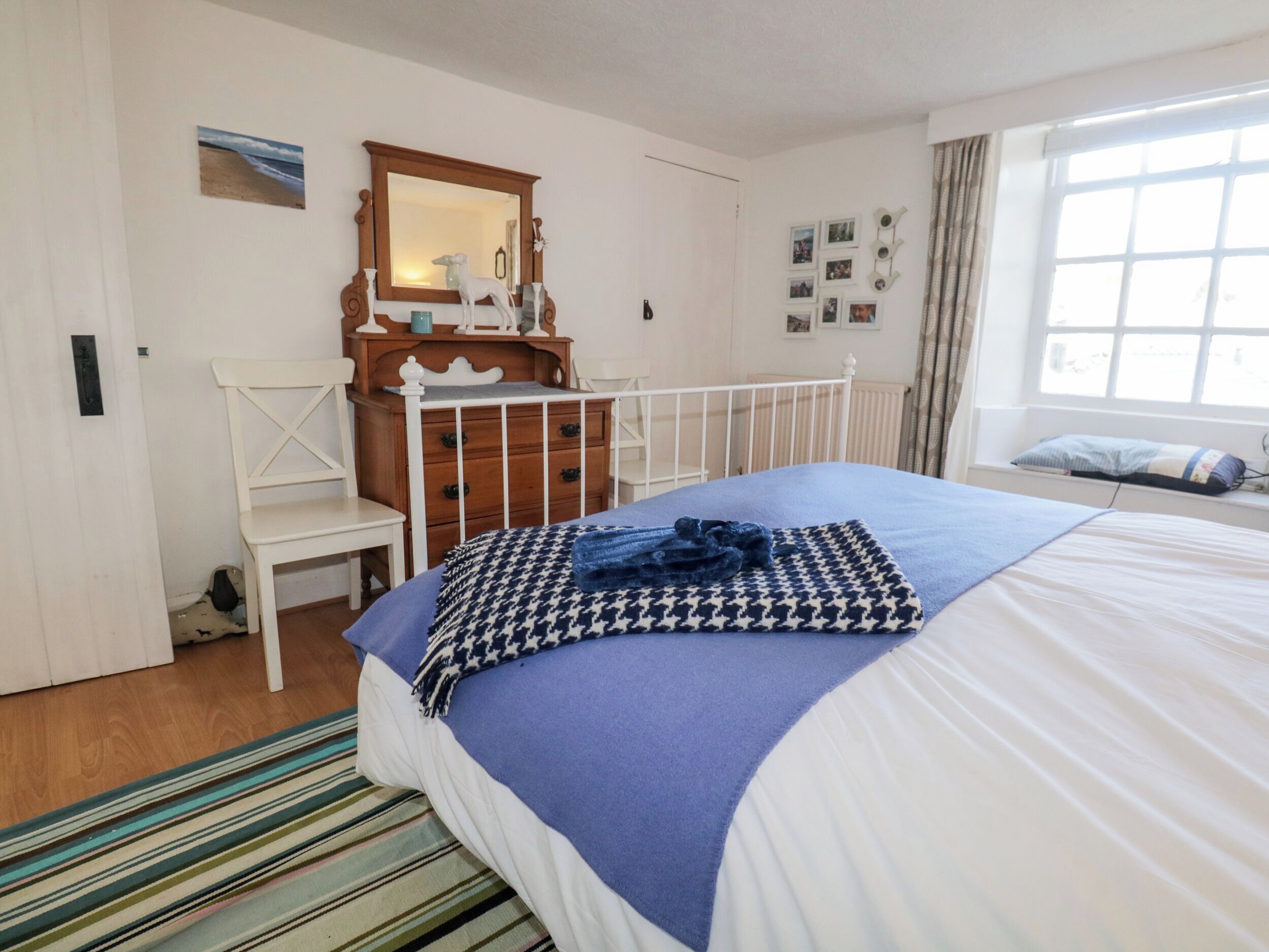 A bedroom with a bed, a dresser, a chair, a mirror, and a window.