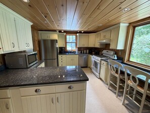 A kitchen with wooden cabinets, a granite countertop, stainless steel appliances, and a window with a view of greenery.