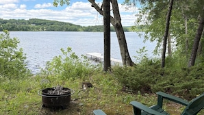 Vista para o lago com um cais, uma lareira e duas cadeiras Adirondack verdes.