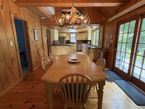 Un intérieur en bois comprenant une table à manger, des chaises, un lustre et de grandes fenêtres.