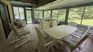 Um alpendre coberto com mesa e cadeiras, um sofá e uma janela com vista para o verde.