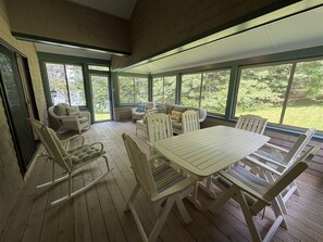 A covered outdoor patio with a table and chairs, a sofa, and a window overlooking greenery.