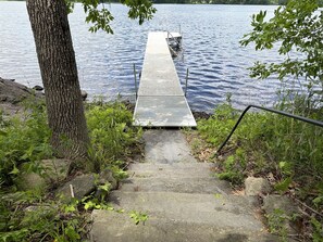 Un escalier en béton menant à une jetée au-dessus de l’eau, entouré de verdure et d’un arbre.