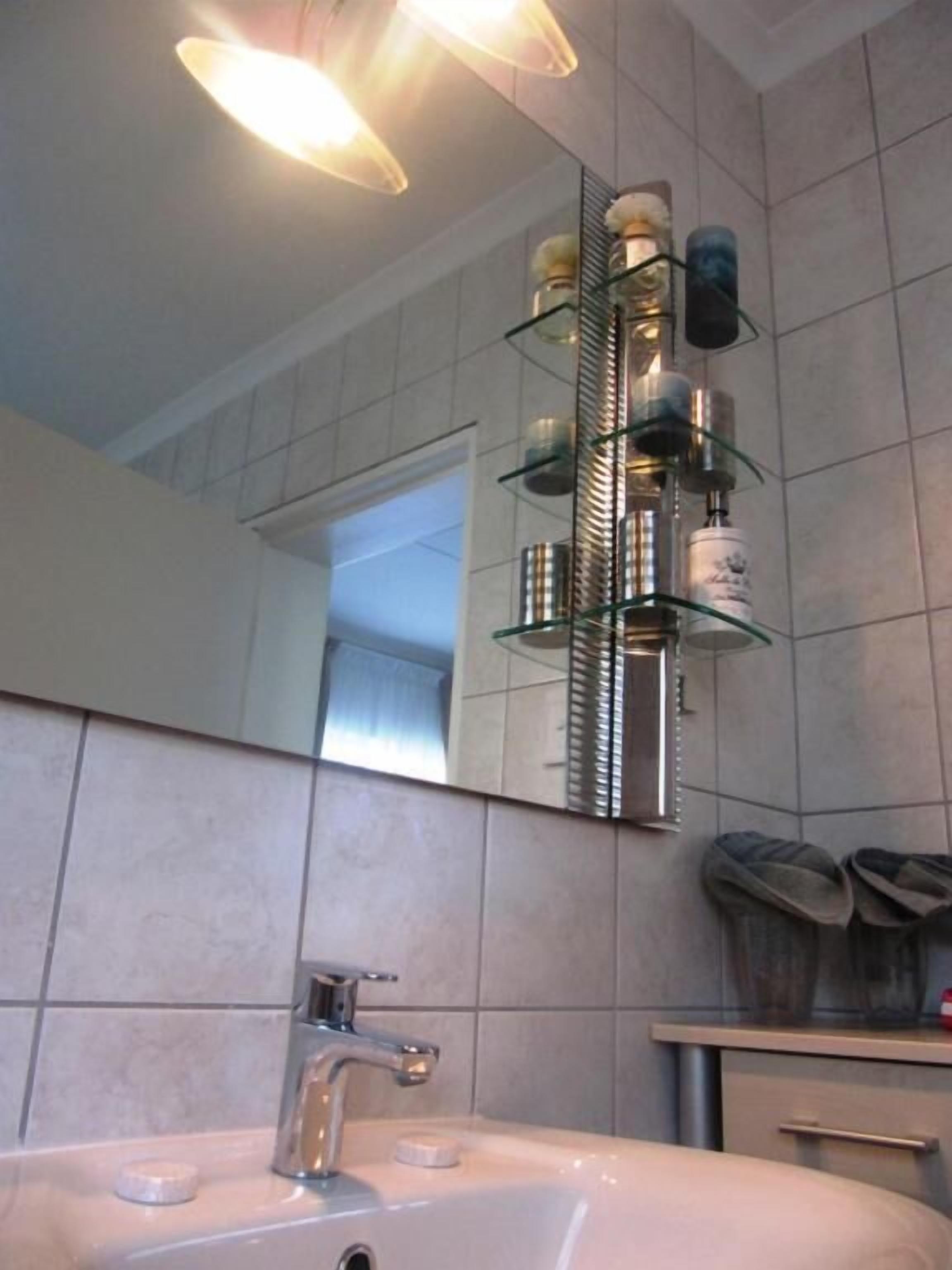 A bathroom with a large mirror, a sink with a modern faucet, and a glass shelf with toiletries.