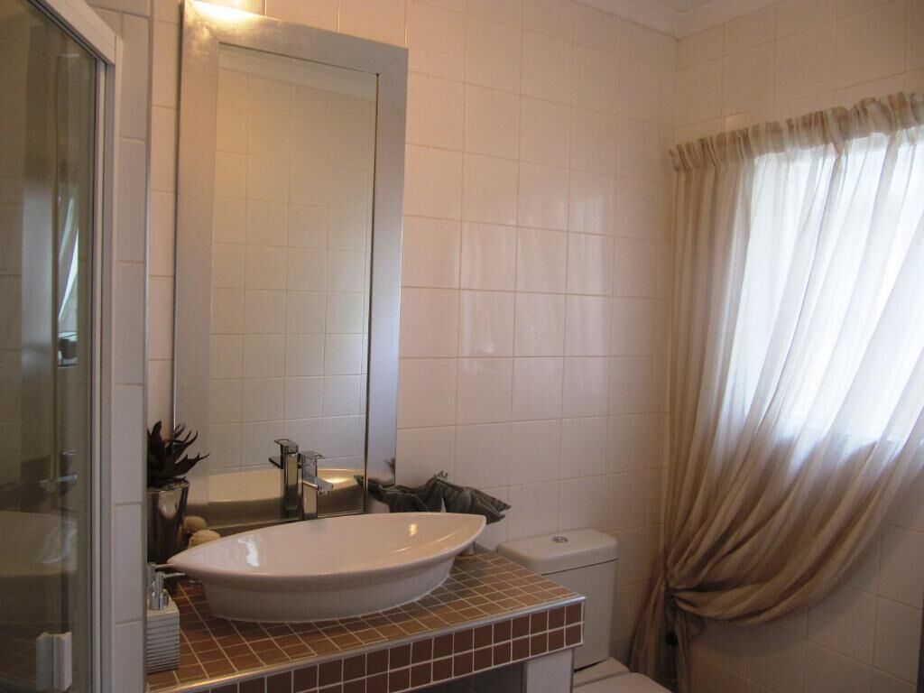 A bathroom with a large mirror, a white sink, a toilet, and a shower area.