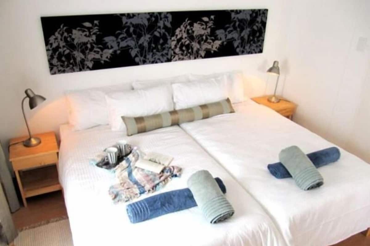 A double bed with white bedding, two pillows, a black and white floral headboard, and two bedside lamps.
