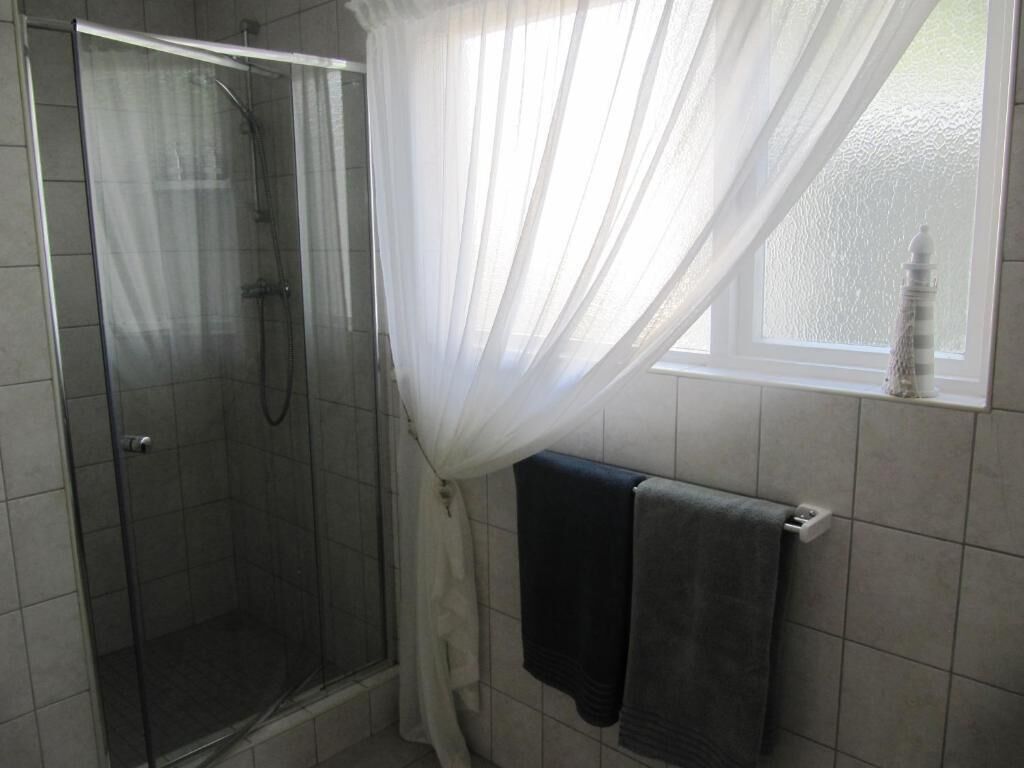 A shower with a glass door, a window with a view, and two towels hanging on a rack.