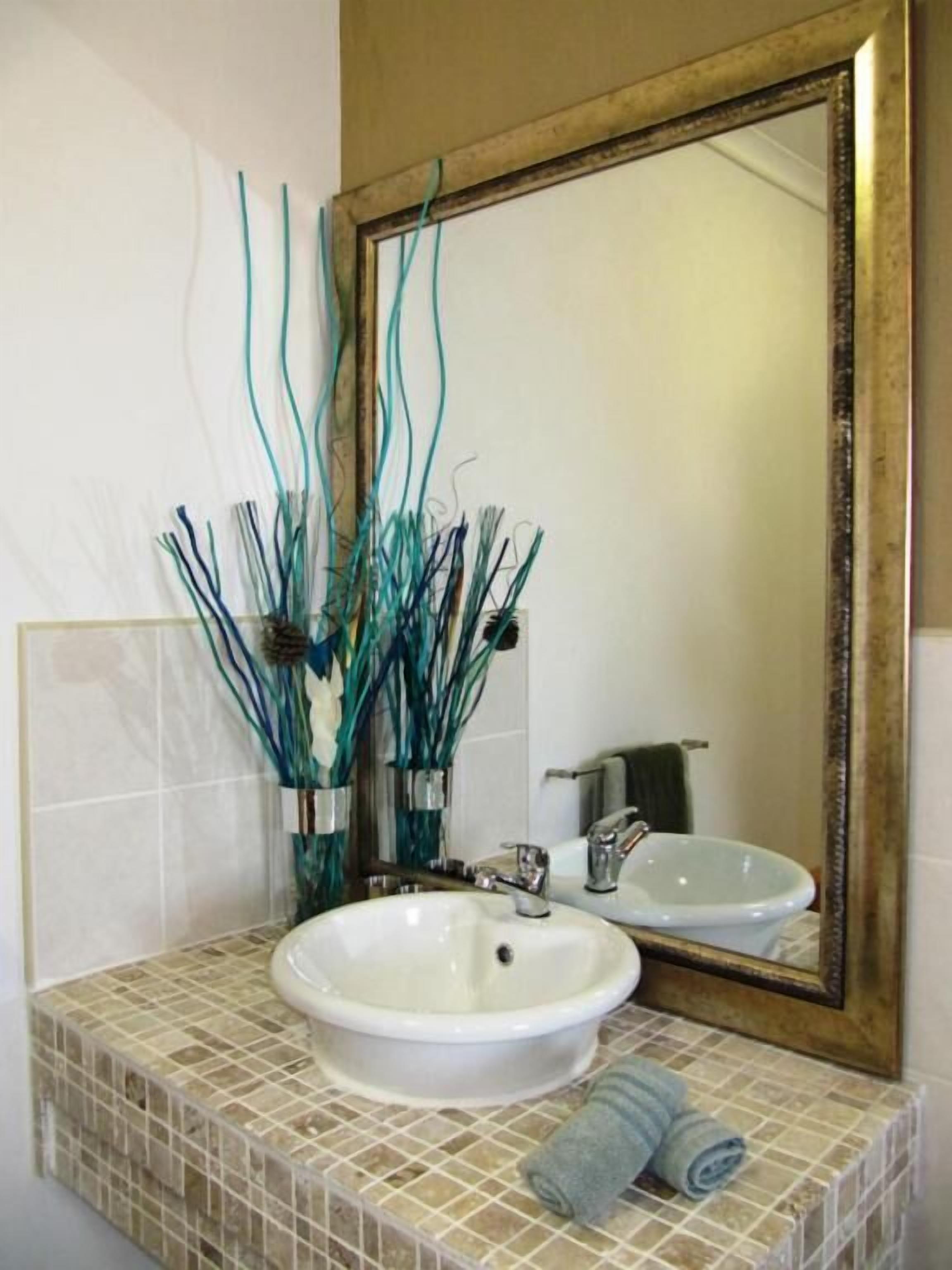 Un baño con lavamanos blanco, espejo con marco dorado y ramas decorativas color turquesa.