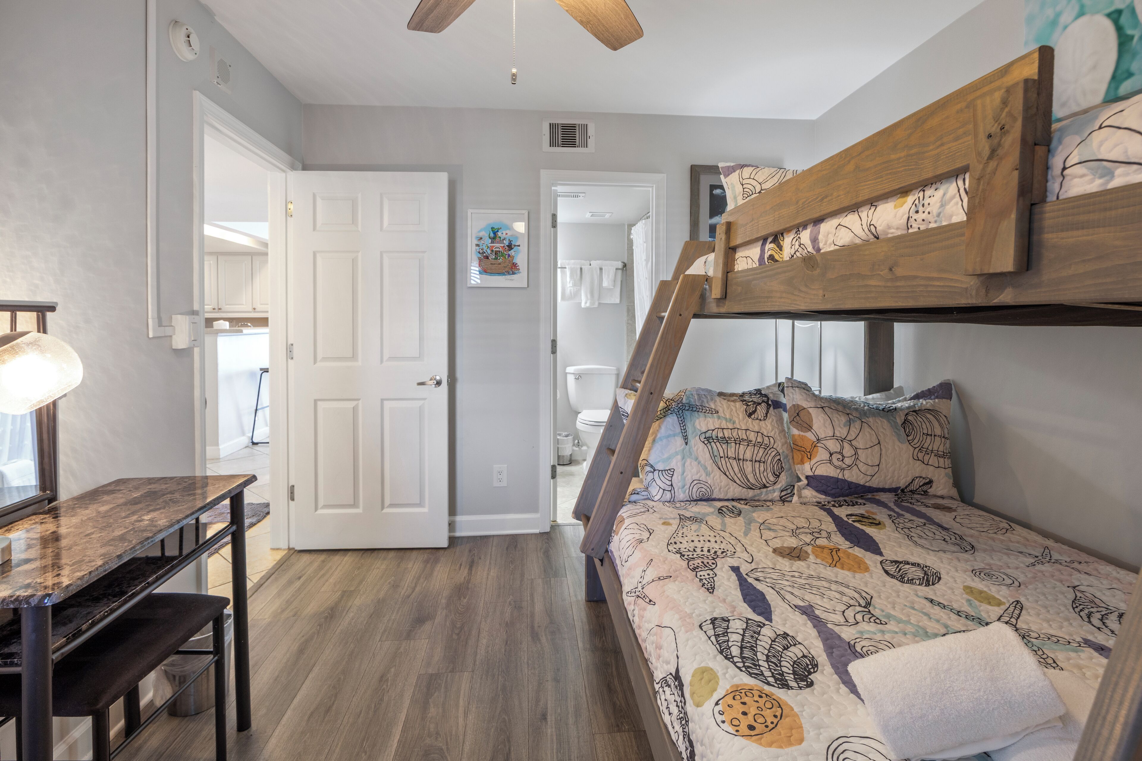 A bedroom with a bunk bed, a desk with a lamp, and a door leading to a bathroom.