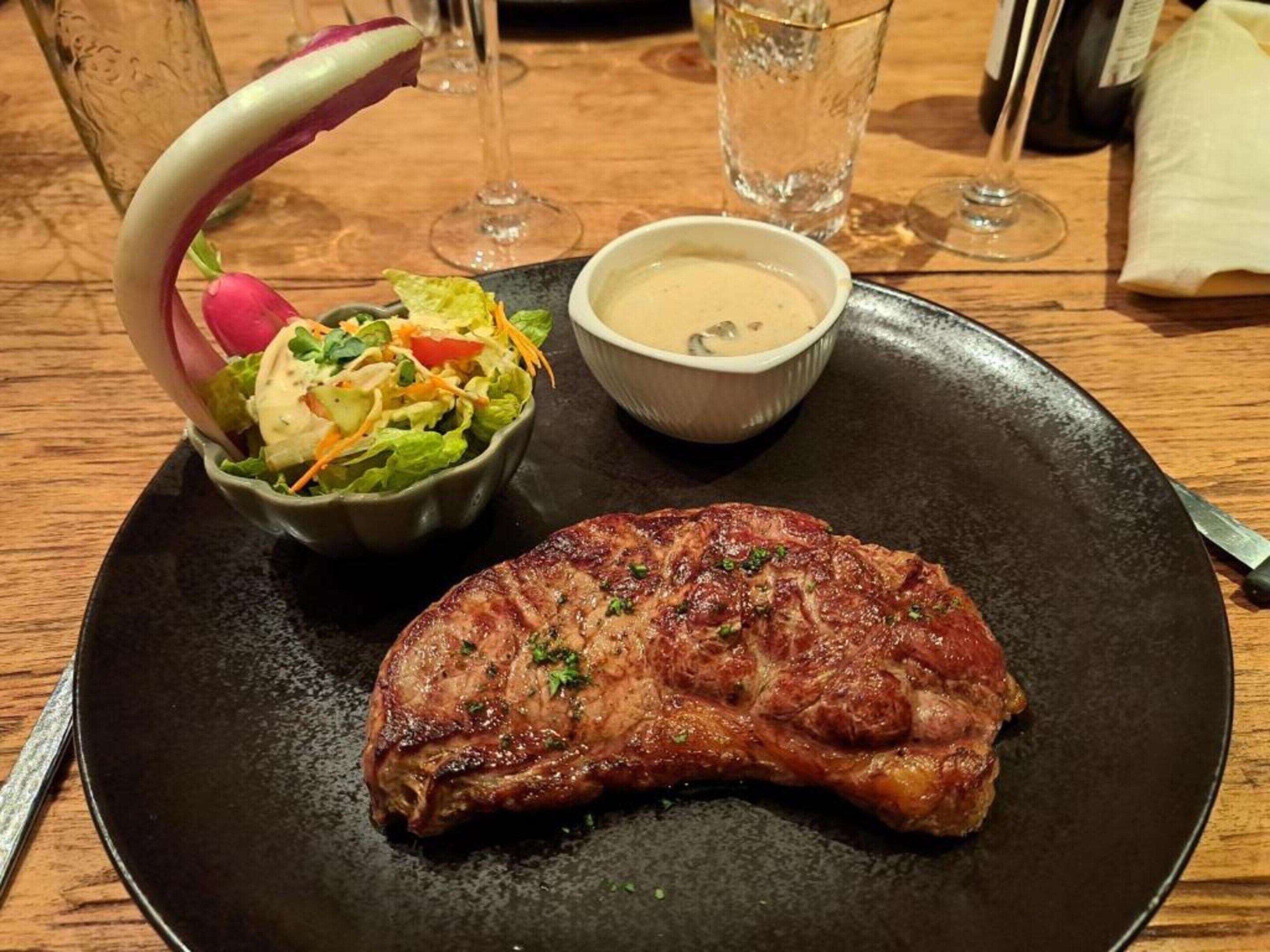 Une assiette avec un steak grillé, une salade en accompagnement et un petit bol de sauce.