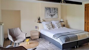 Un dormitorio con cama, una silla, una mesita de noche, una lámpara y un cuadro en la pared.