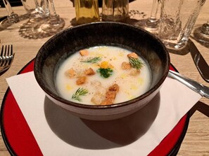 Un plato de sopa con croutons y hierbas, sobre un mantel individual rojo y blanco.