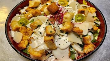 A bowl of salad with croutons, cheese, and a creamy dressing.