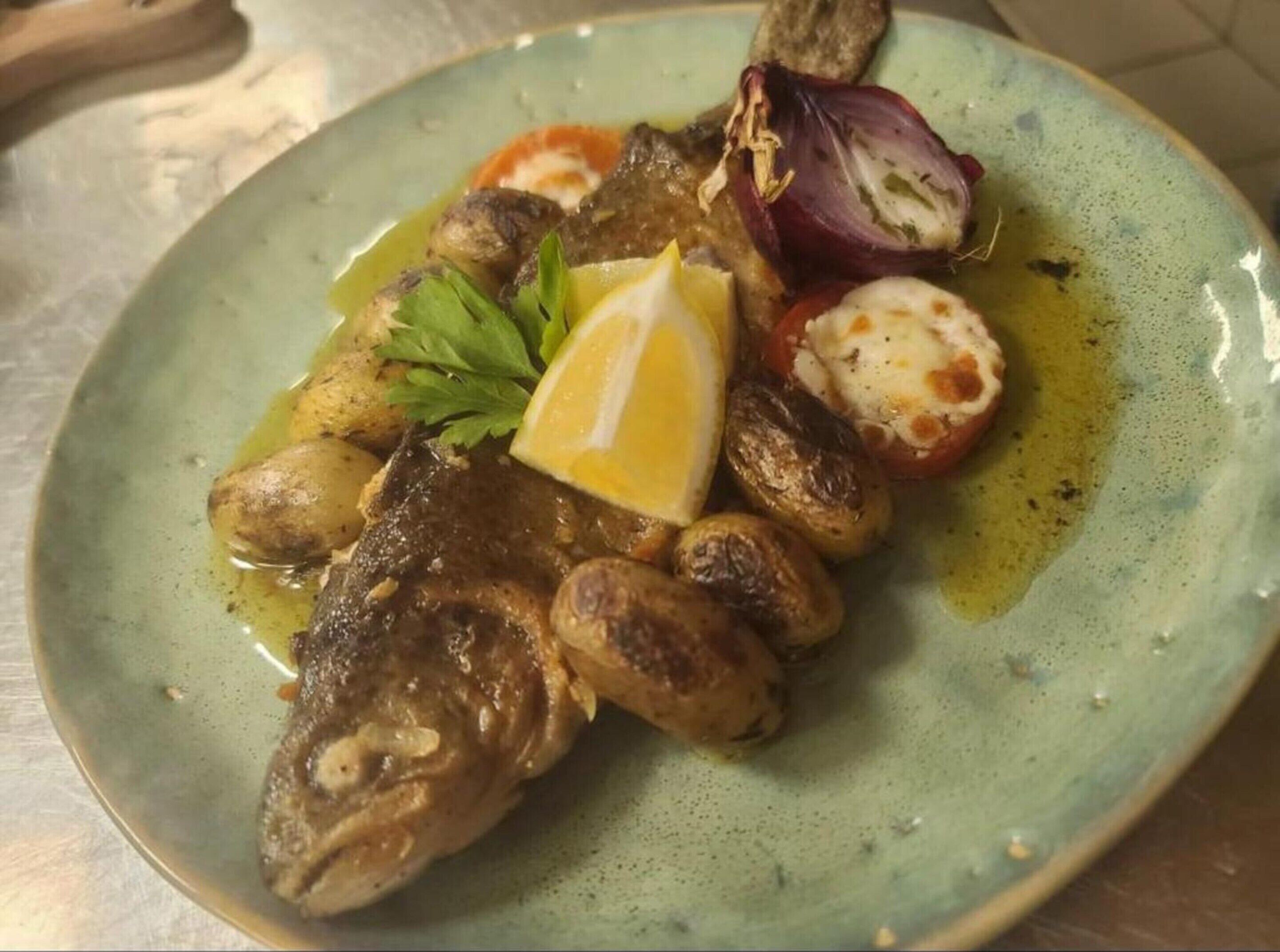 Un plato con pescado, patatas, tomates y una cuña de limón.