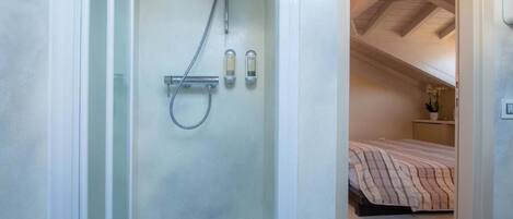 A compact bathroom with a shower, a toilet, and a small bedside table with a plant.