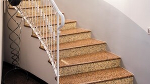Uma escadaria curva com degraus de granito e balaústres brancos, que leva a um patamar com obras de arte emolduradas na parede.