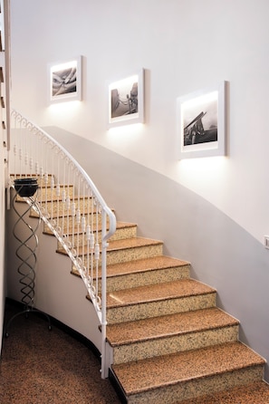 A curved staircase with granite steps and white balusters, leading to a landing with framed artwork on the wall. - Hotel Don Ferrante (Bellagio)