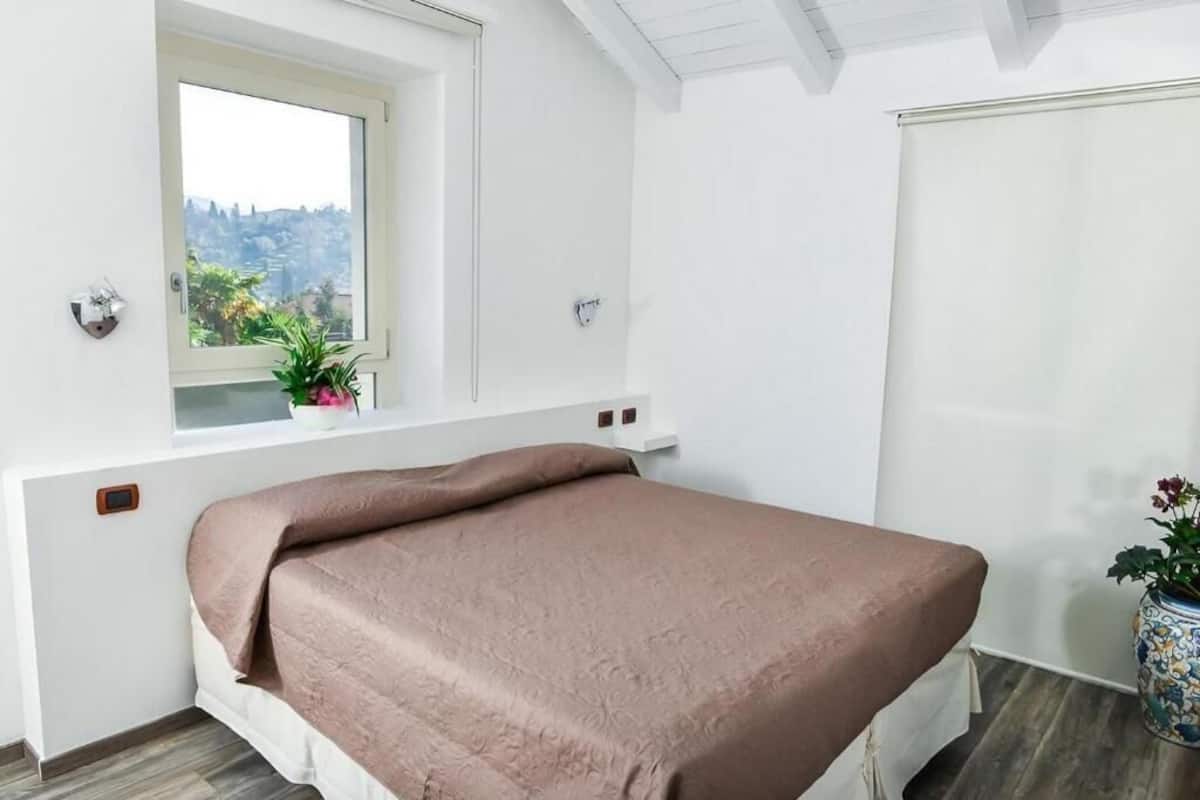 A bedroom with a bed, a window with a view, a potted plant, and a door.