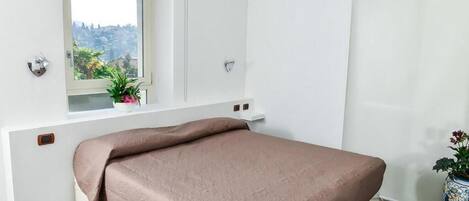 Ein Schlafzimmer mit Bett, Fenster mit Blick, einer Topfpflanze und einer Tür.