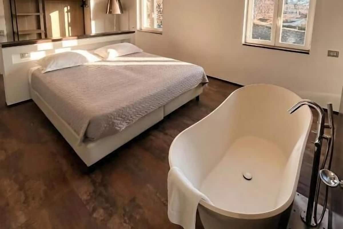 A modern bedroom with a large bed, a built-in wardrobe, and a freestanding bathtub.