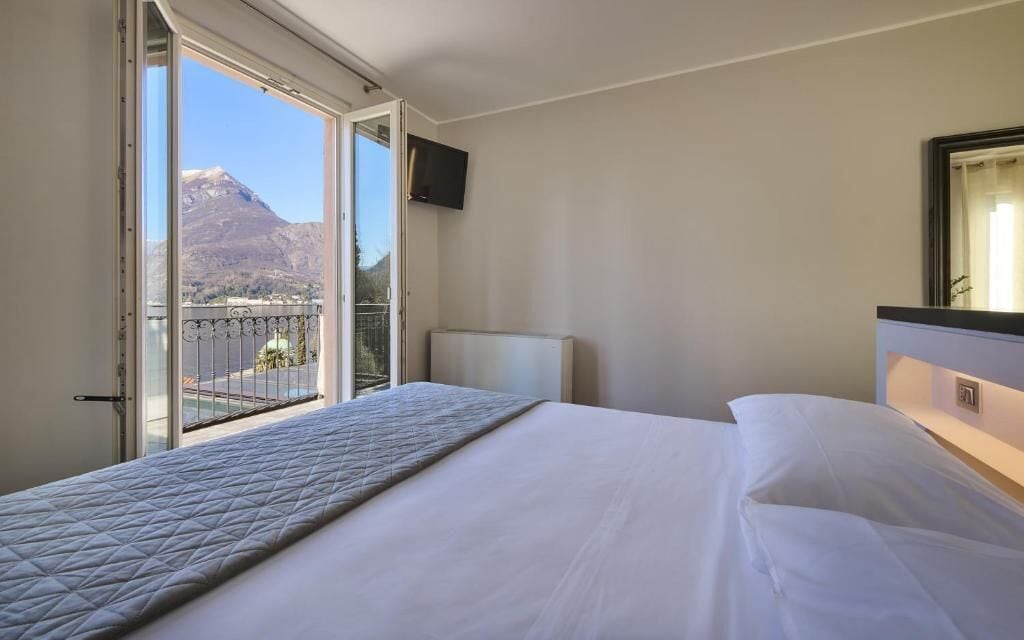 Habitación de hotel con cama, televisor en la pared y balcón con vista a la montaña.