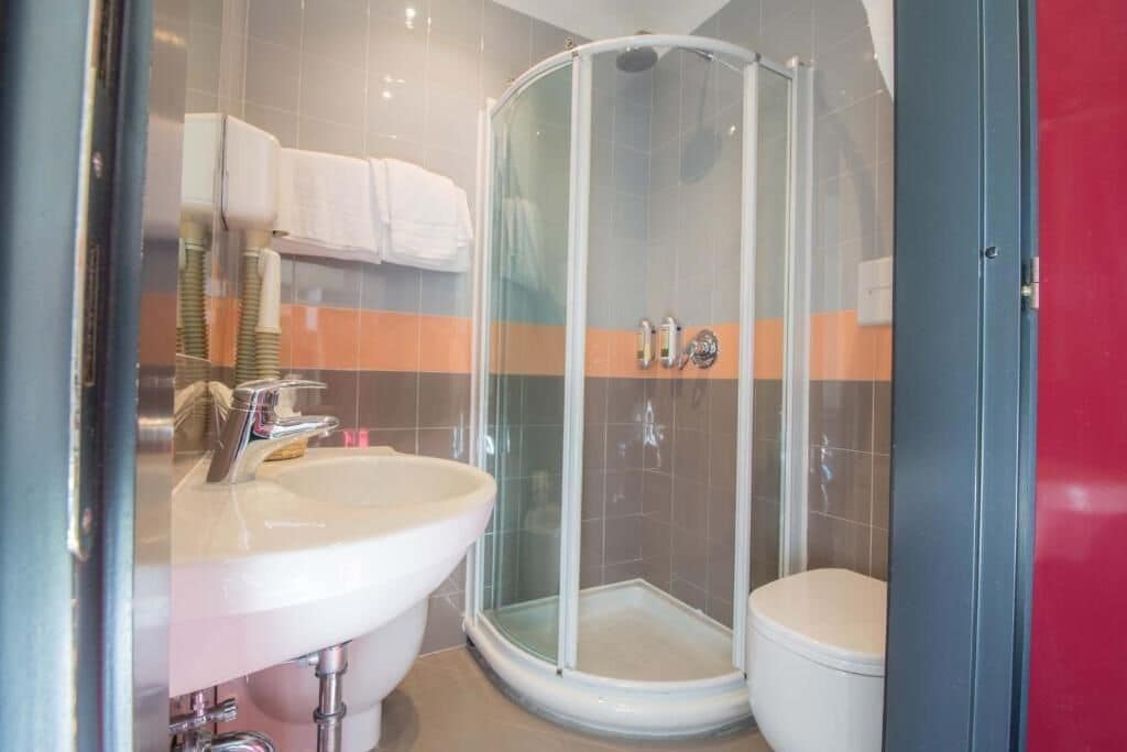 Un baño moderno con ducha envuelta en vidrio, un lavamanos blanco y un inodoro.