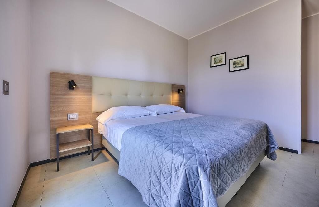 Une chambre à coucher moderne avec un grand lit, une tête de lit en bois, des lampes de chevet et deux tableaux encadrés accrochés au mur.