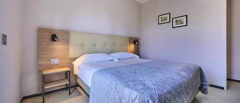 A modern bedroom with a large bed, a wooden headboard, bedside lamps, and two framed pictures on the wall.