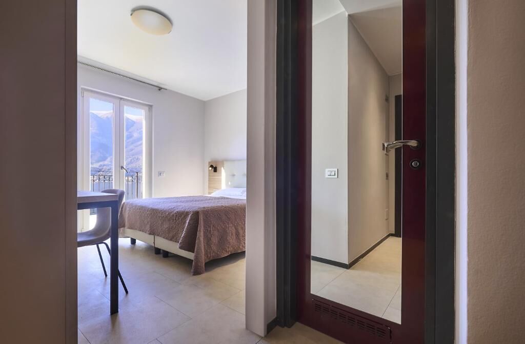 A hotel room with a bed, a small table, and a chair. There is a window with a view of mountains.