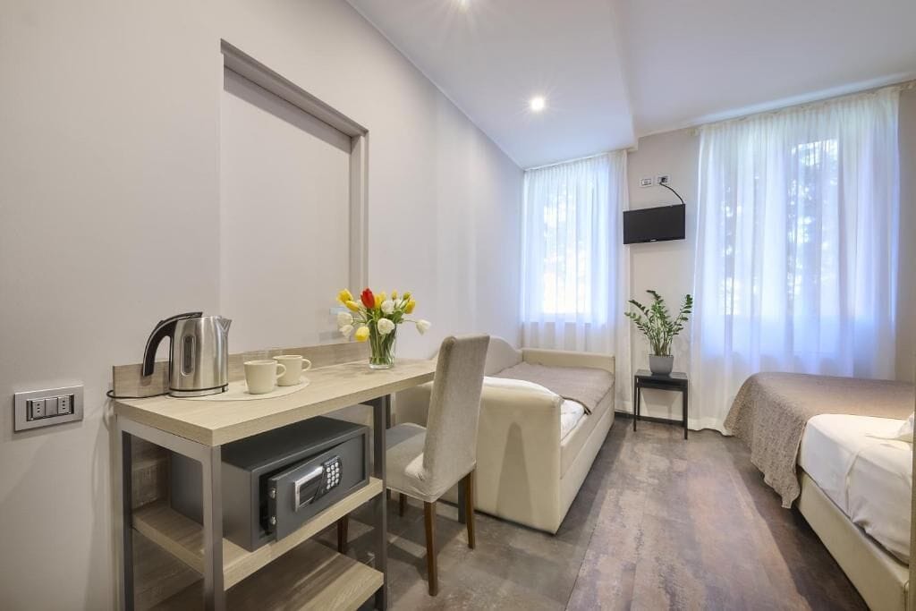 A hotel room with a desk, chair, bed, TV, and a small table with a plant.