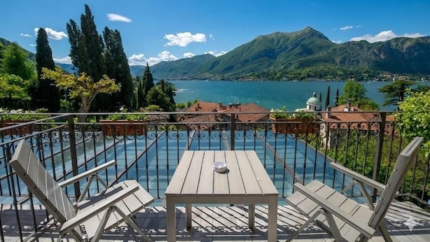Um terraço com mesa e cadeiras, com vista para um lago, rodeado por montanhas e árvores.