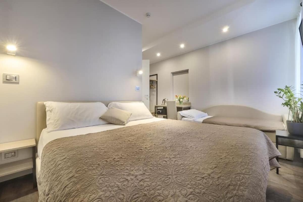 A modern bedroom with a large bed, bedside tables, a mirror, and a potted plant.