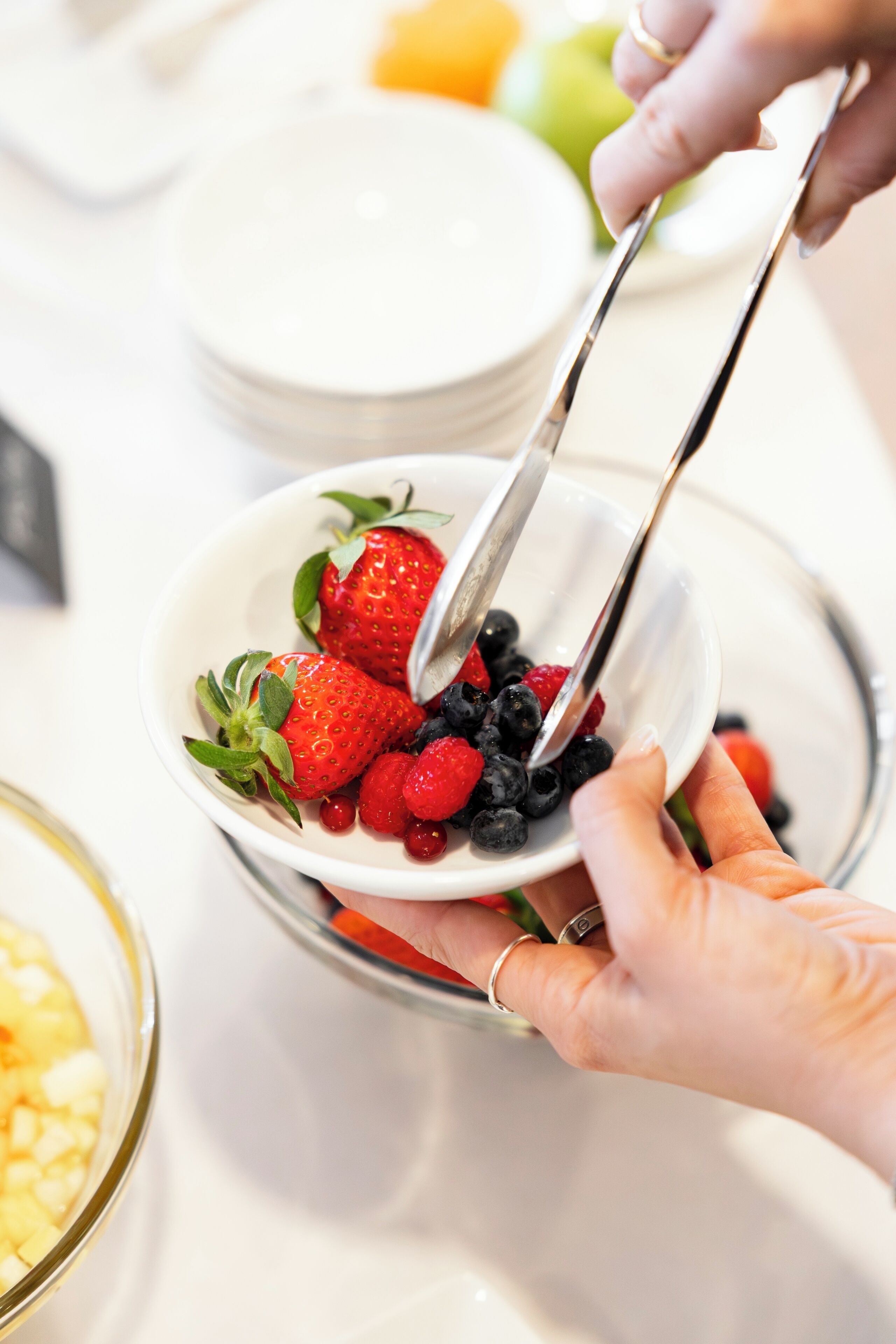A person serving a bowl of mixed berries.