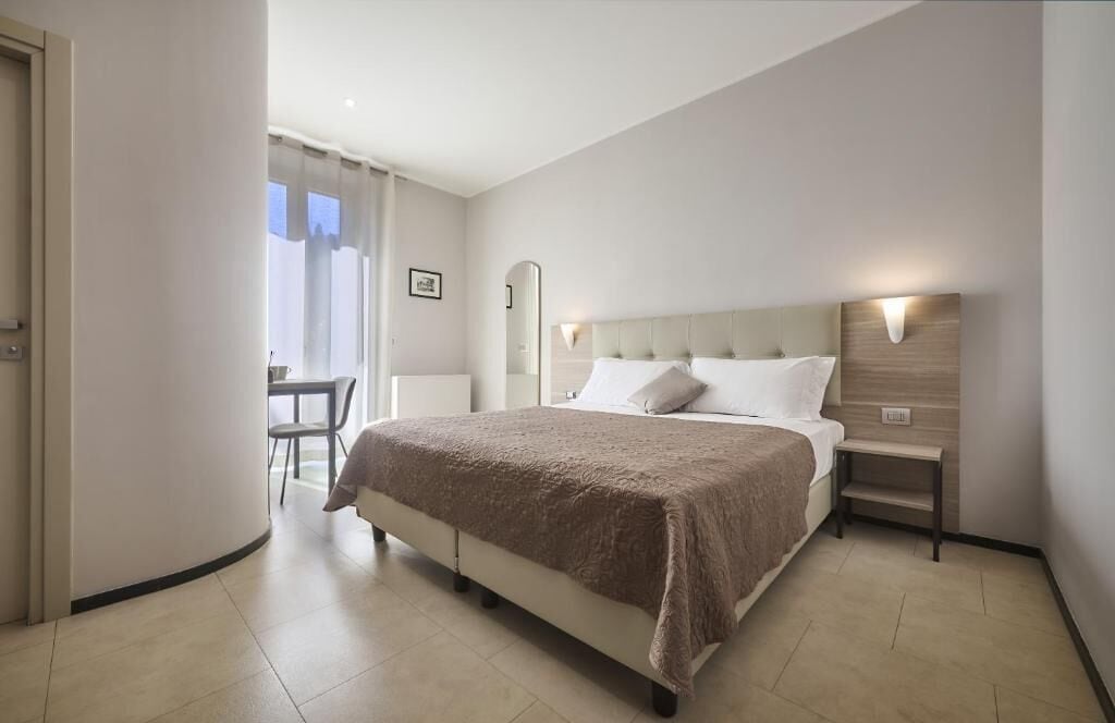 A hotel room with a large bed, a bedside table, a chair, and a desk.