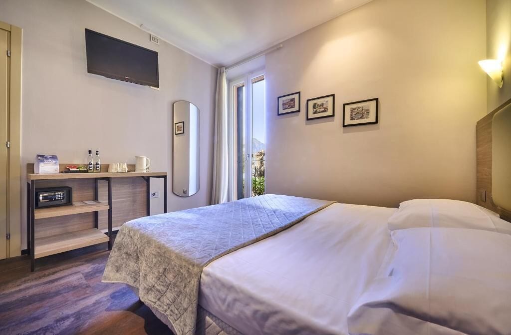 Una habitación de hotel con una cama, un escritorio con espejo, un televisor y una ventana con cortinas.
