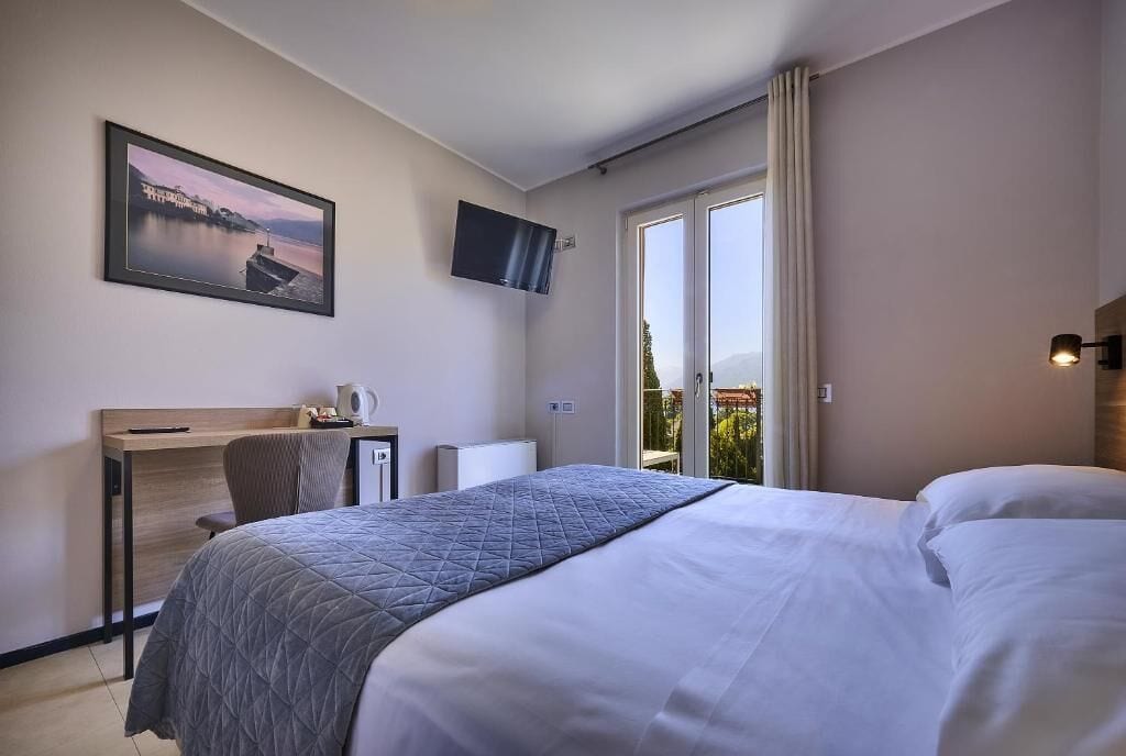 Ein Hotelzimmer mit einem Bett, einem Schreibtisch mit Stuhl, einem Fernseher und einem Fenster mit Vorhängen.