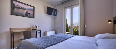 Habitación de hotel con cama, escritorio con silla, televisión y ventana con cortinas.