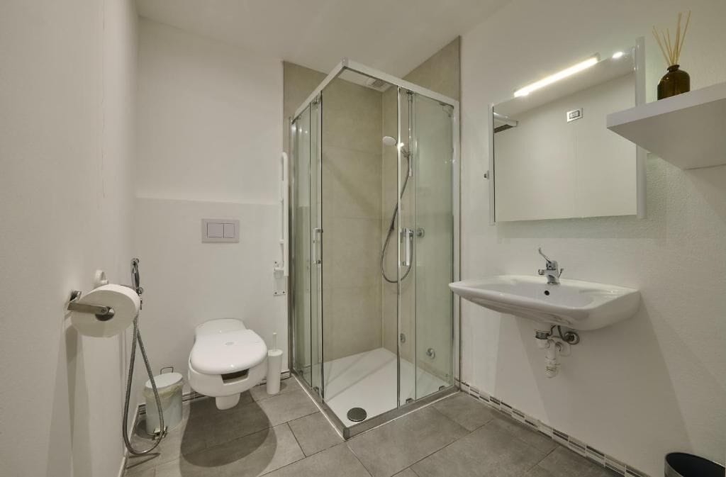 Un baño moderno con ducha de vidrio, lavamanos blanco y retrete.