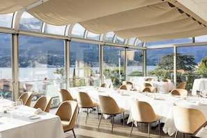 A restaurant with tables set for dining, large windows, and a view of mountains and water.