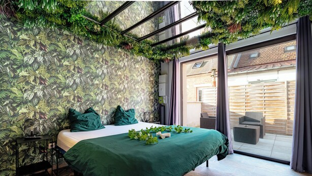 A bedroom with a bed, green bedding, a nightstand, and a wall with a leafy pattern.