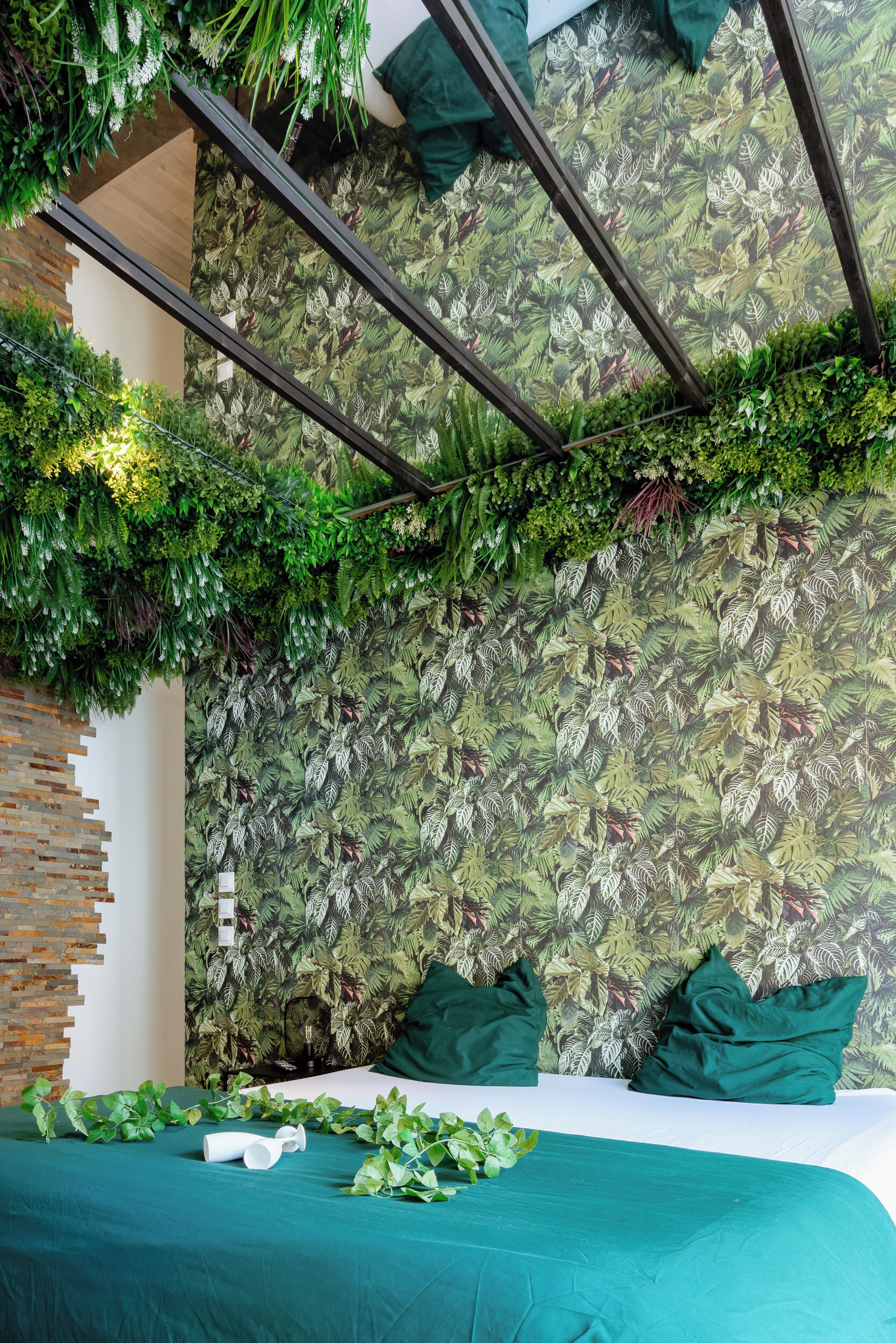 Une chambre avec un lit, une literie verte, un mur orné d’un motif de feuilles et un mur fait de lattes de bois.