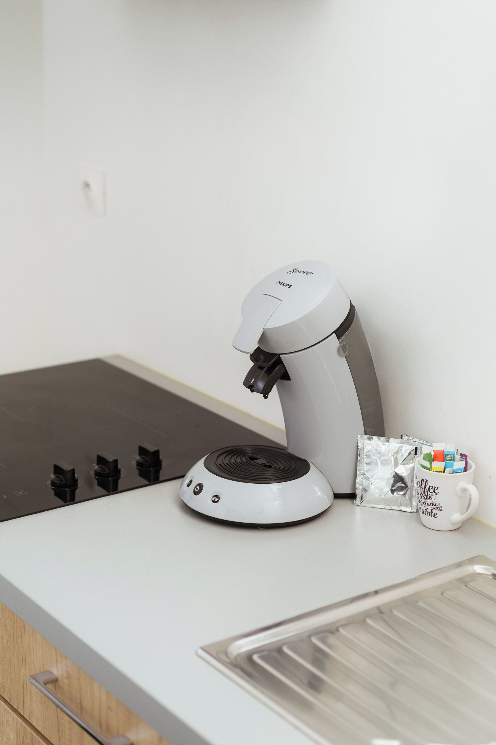 A coffee machine on a white countertop with a coffee mug and packets of coffee pods.