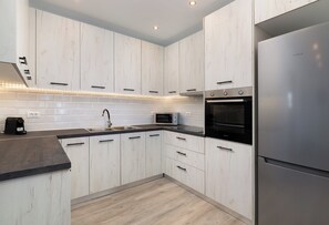 A modern kitchen with white cabinetry, a stainless steel refrigerator, a microwave, and an oven. - Black Stone Apartment (Kremasti)