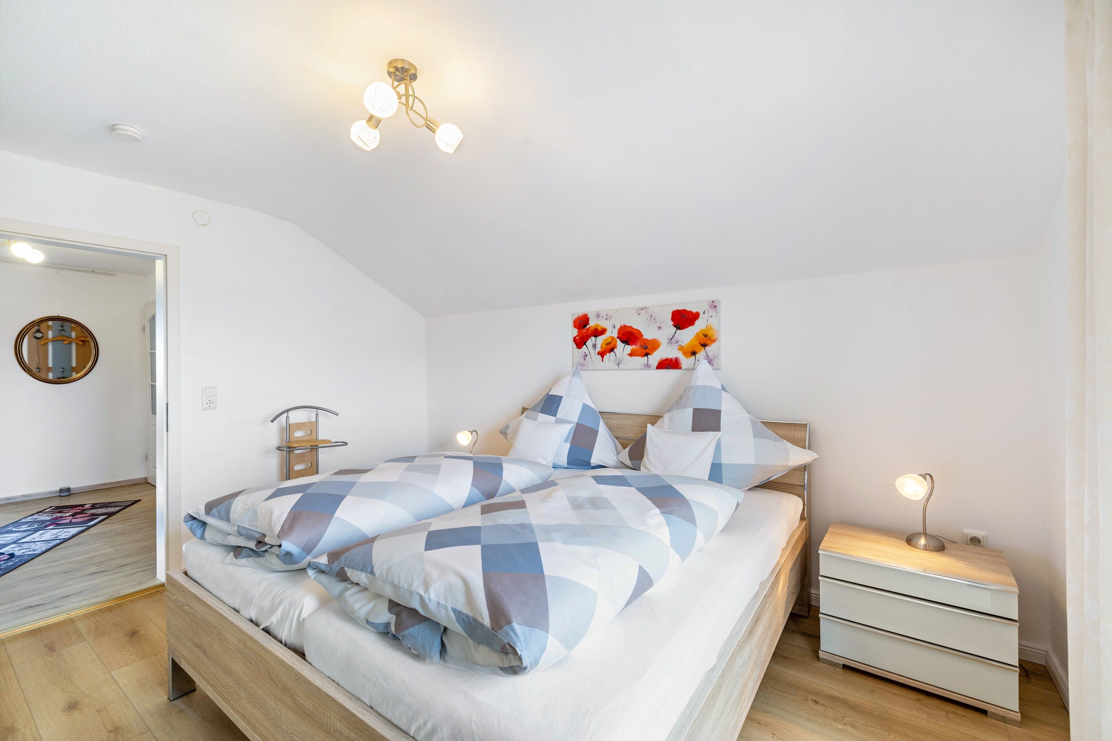 A bedroom with a bed, bedside tables, a nightstand, a wall-mounted light fixture, and a door.