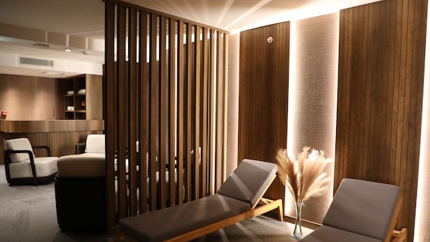 Un espace de détente moderne comprenant deux fauteuils, un paravent en bois et une petite table décorée de plumes d’herbe de la pampa.