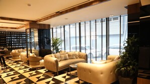 A modern lobby with a geometric floor pattern, plush seating, large windows, and a view of the sea. - PL Managed By Dedeman (Istanbul)