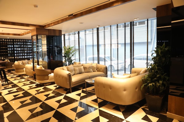 Eine moderne Lobby mit geometrischem Bodenmuster, komfortablen Sitzgelegenheiten, großen Fenstern und Meerblick.