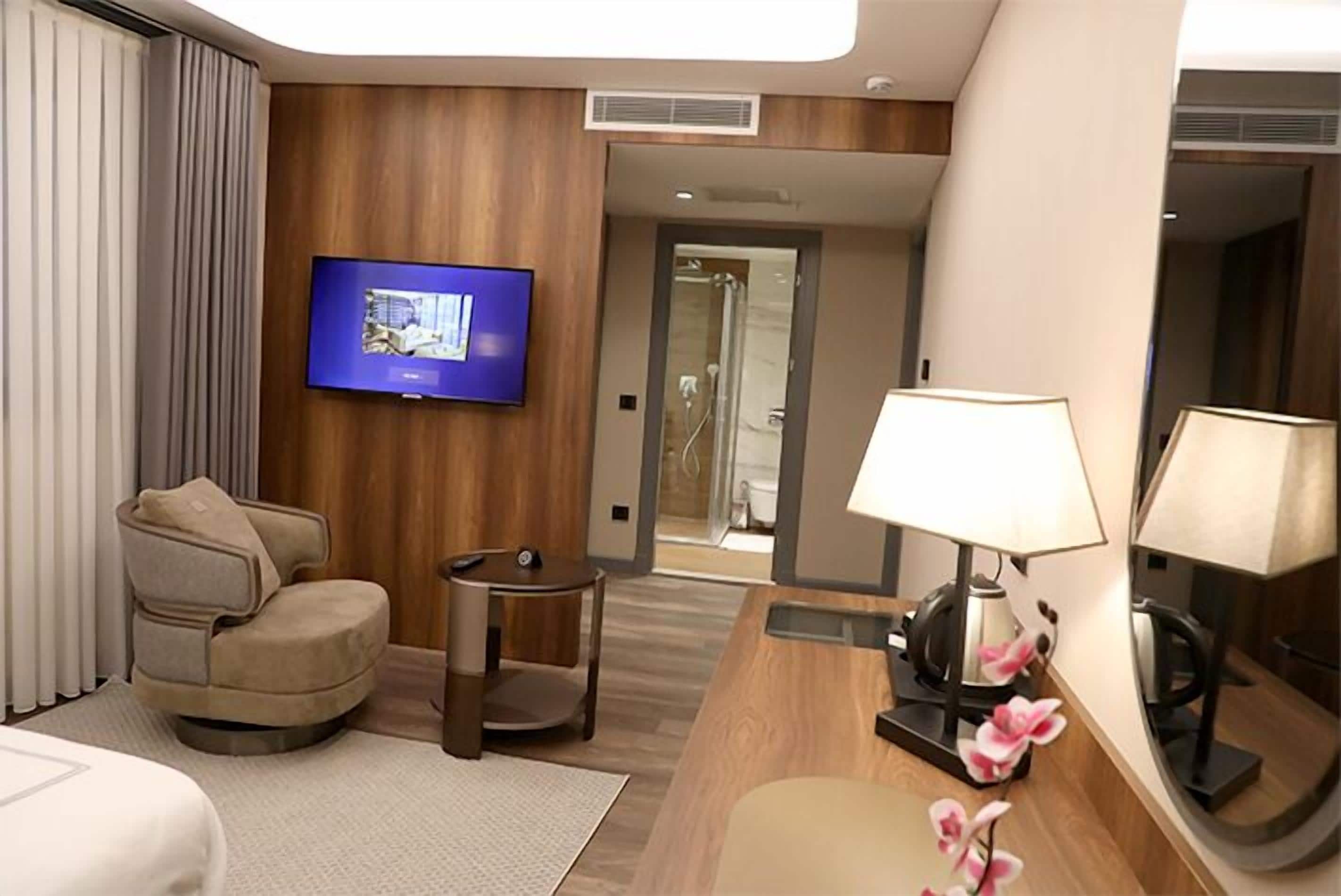 Une chambre d’hôtel équipée d’une télévision à écran plat, d’un canapé, d’une petite table, d’une lampe et d’un miroir.